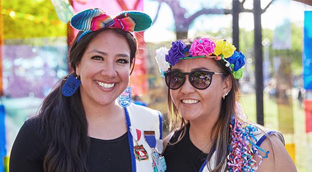 Two women dressed up in fiesta ribbons and sashes and smiling